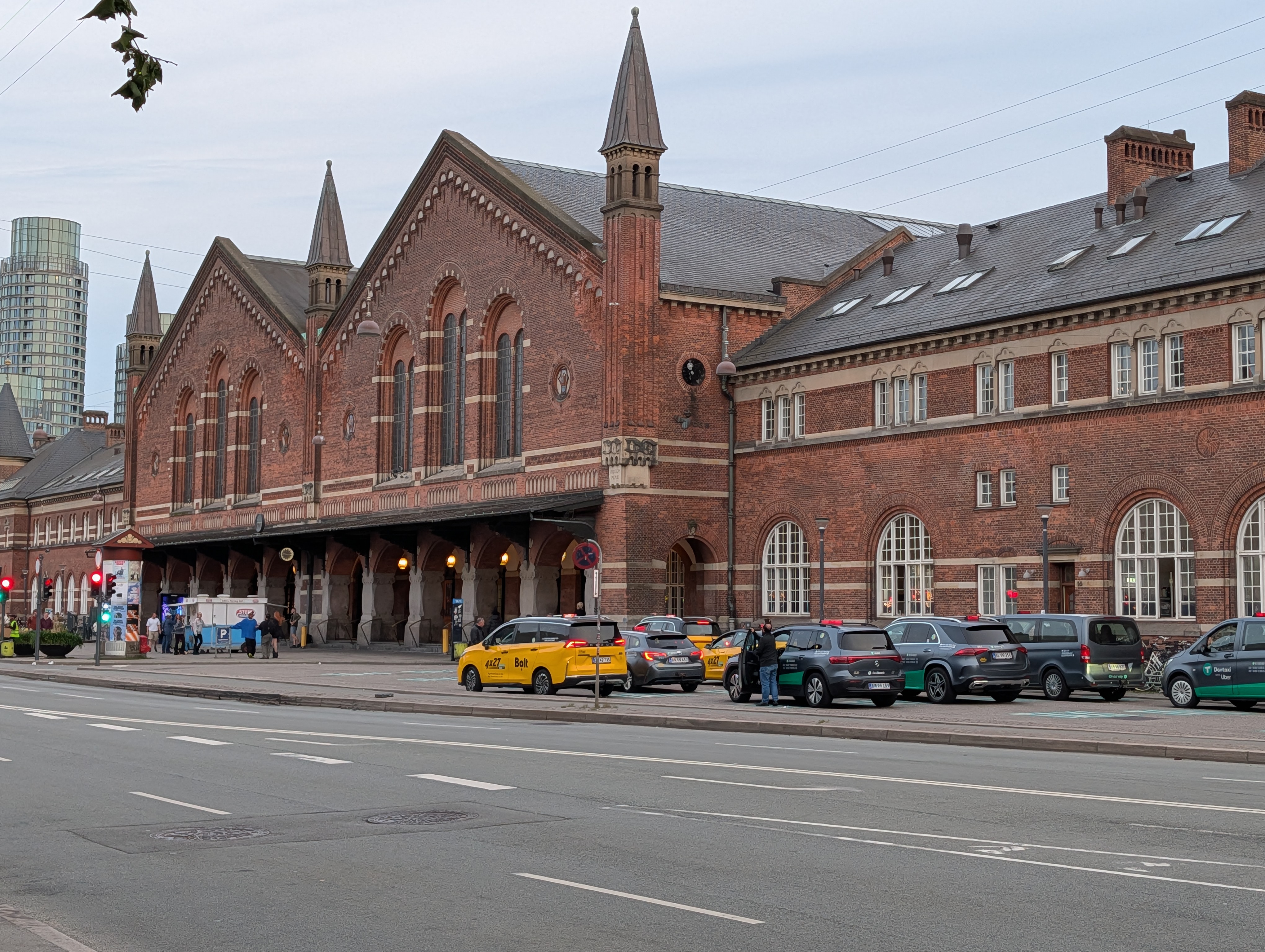 Københavns hovudbanegard i raud teglstein sett frå gata med drosjer og bilar parkerte framfor inngangen.